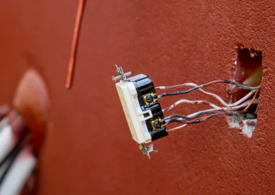 Exposed electrical outlet with wiring on a red wall.