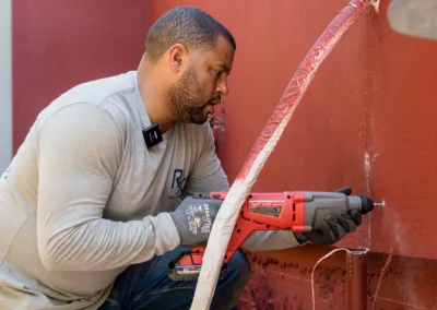 A man using a power drill on an exterior wall for an installation or repair.