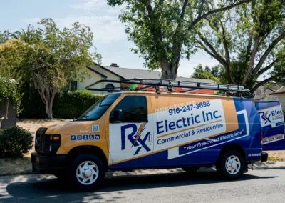 A blue and white commercial electrician service van parked on a sunny suburban street.