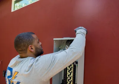 A technician is installing or repairing an electrical panel on a red wall.