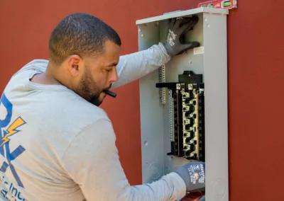 A technician installing or servicing an electrical panel on a red wall.