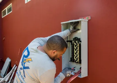 An electrician is installing or servicing an electrical panel on a red wall.