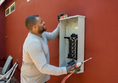 Electrician installing a circuit breaker panel on a red wall.