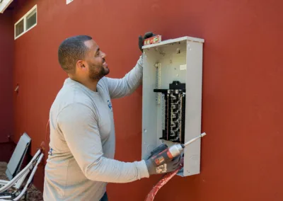 An electrician installing or repairing an electrical panel on an exterior wall.