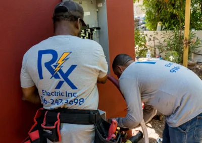 Two electricians working on an outdoor electrical panel.