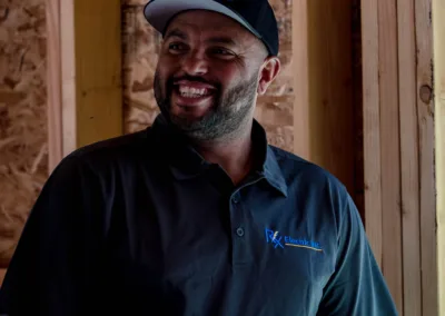 Man in a cap smiling inside a building with unfinished wooden walls.