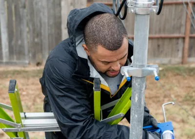 A man using a caulk gun to apply sealant around a base of a metal post outdoors.