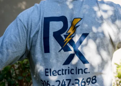 A person wearing a company t-shirt with a logo that reads "rx electric inc." and contact information.