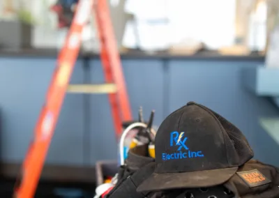 An electrician's hard hat and tools in focus, with the electrician working on a ladder in the background.