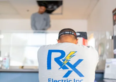 Worker wearing a shirt with the logo of rx electric inc. while another person works on the ceiling.