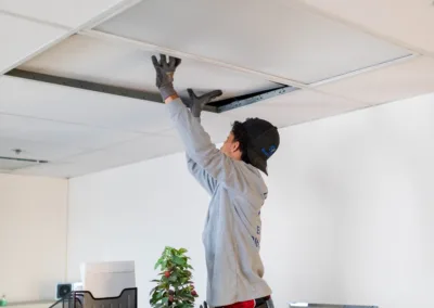 Person on a stepladder installing ceiling tiles in an office.