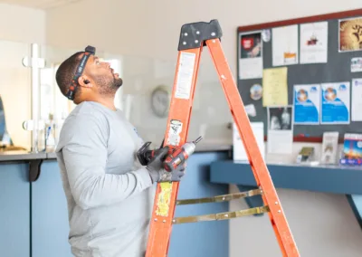 A man standing on a ladder while looking upwards, possibly inspecting or fixing something above.