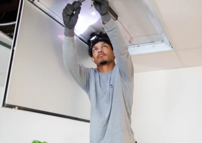 A person working on ceiling-mounted electrical fixtures while standing on a stool.