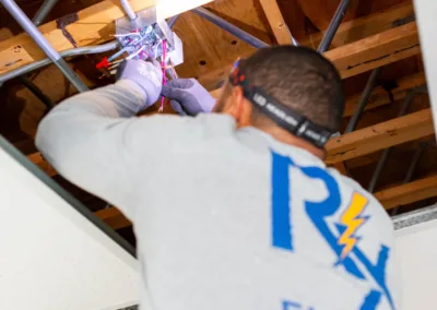 An electrician working on wiring in an attic space.