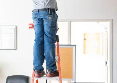 A worker standing on a ladder to access the ceiling, possibly performing maintenance or installation work.