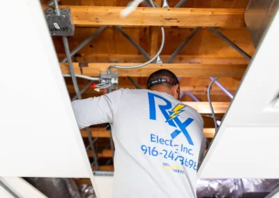 Electrician working on wiring in an attic space.