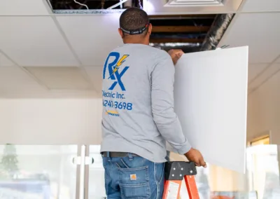 Worker on a ladder performing maintenance on an hvac system above ceiling tiles.