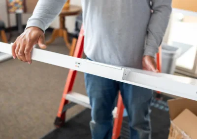 Man holding a metal beam with measurement markings in a room with construction materials.