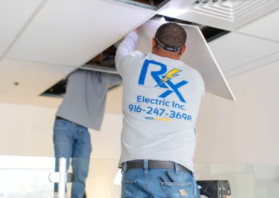 Two electricians working on ceiling installations, one reaching into the ceiling cavity.