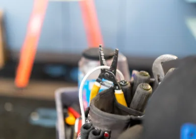 A toolbox filled with various tools in focus, with a blurred ladder in the background indicating a work or construction environment.